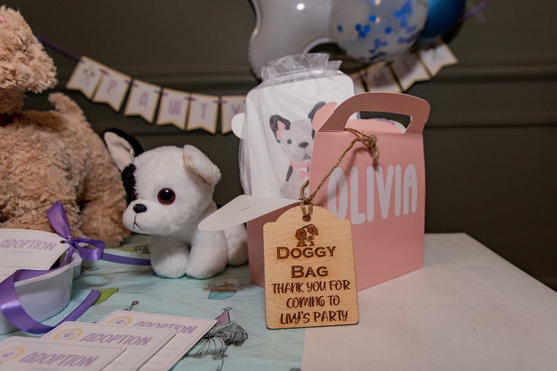 Peut inclure: Sc&egrave;ne de f&ecirc;te avec un jouet en peluche chien blanc et noir, un sac cadeau rose avec "OLIVIA" imprim&eacute; dessus, et une &eacute;tiquette en bois avec "DOGGY BAG THANK YOU FOR COMING TO LIV'S PARTY". Des cartes sur le th&egrave;me de l'adoption sont &eacute;galement pr&eacute;sentes.