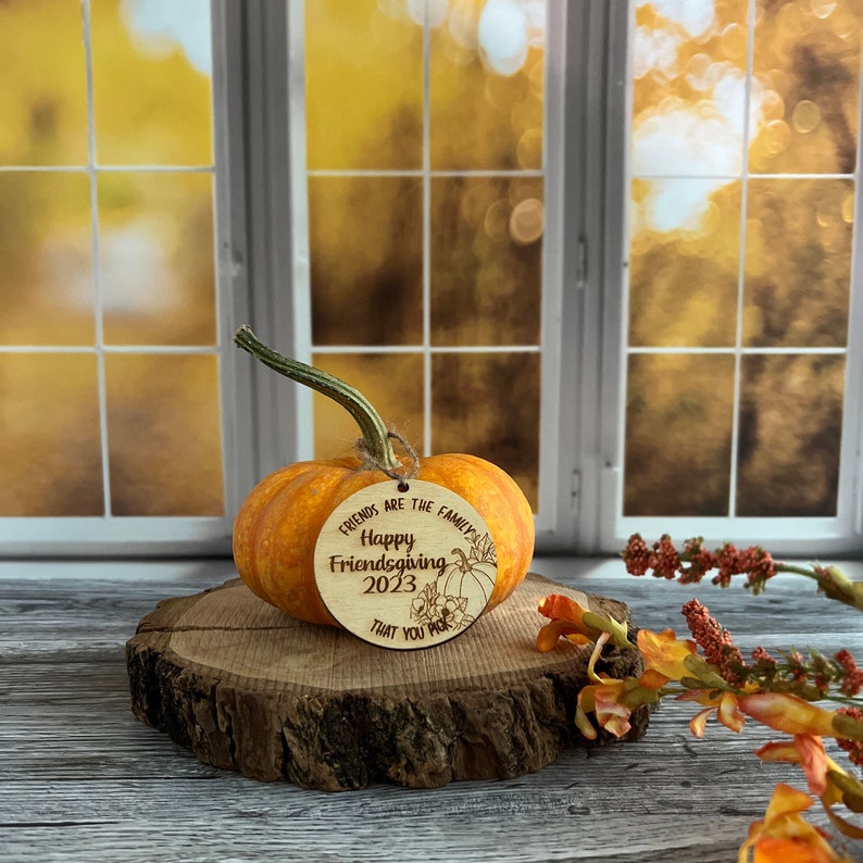 May include: A small orange pumpkin with a wooden tag that reads "Friends are the family you pick. Happy Friendsgiving 2023".