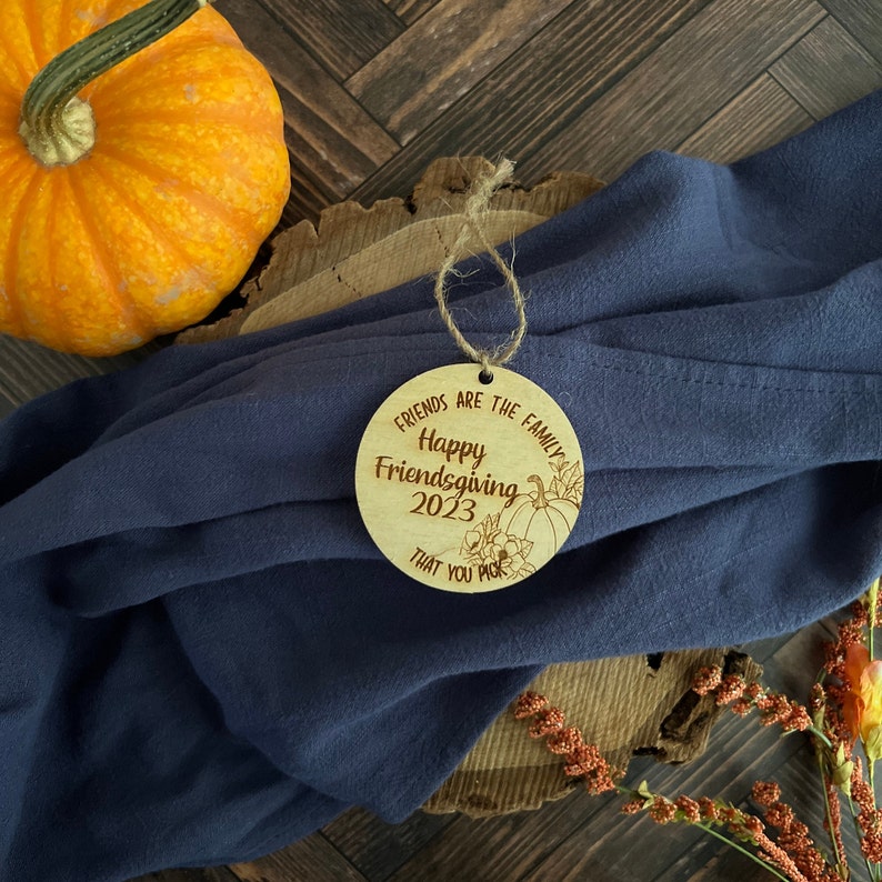 May include: A round wooden ornament with the text "Friends are the family. Happy Friendsgiving 2023 that you pick" and a pumpkin design.