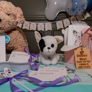 Peut inclure: Sc&egrave;ne de f&ecirc;te avec des peluches de chiots, des certificats d'adoption et une bo&icirc;te &agrave; cadeaux rose "Doggy Bag". La sc&egrave;ne comprend une banni&egrave;re et des ballons, cr&eacute;ant une atmosph&egrave;re festive pour un &eacute;v&eacute;nement sur le th&egrave;me des chiots.