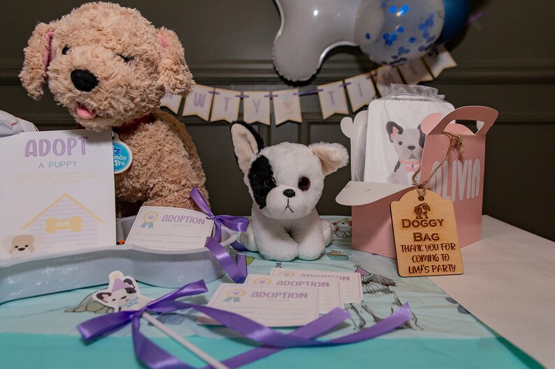 Peut inclure: Sc&egrave;ne de f&ecirc;te avec des peluches de chiots, des certificats d'adoption et une bo&icirc;te &agrave; cadeaux rose "Doggy Bag". La sc&egrave;ne comprend une banni&egrave;re et des ballons, cr&eacute;ant une atmosph&egrave;re festive pour un &eacute;v&eacute;nement sur le th&egrave;me des chiots.