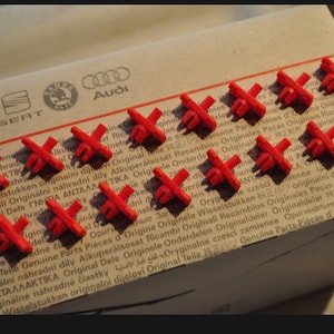 May include: A close-up of a box with a variety of red plastic clips. The box is labeled with the logos of various car brands, including Volkswagen, Seat, Skoda, and Audi. The text on the box reads "Original Teile Genuine Parts Pièces d'Origine Originale Wisselstukken 純正 originalni dijelovi Original Teile".