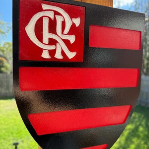 Peut inclure: Un panneau en bois en forme de bouclier noir et rouge avec un logo "CR" blanc dans le coin sup&eacute;rieur gauche. Le bouclier a une bordure noire et des rayures rouges et noires.