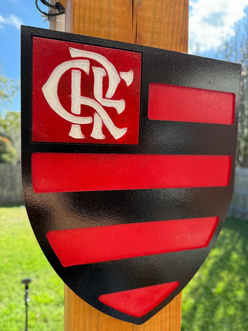 Peut inclure: Un panneau en bois en forme de bouclier noir et rouge avec un logo "CR" blanc dans le coin sup&eacute;rieur gauche. Le bouclier a une bordure noire et des rayures rouges et noires.