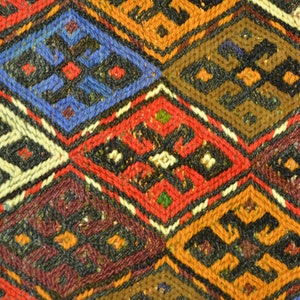 May include: Close-up of a woven textile with a repeating diamond pattern. The design features various colors, including red, blue, orange, brown, and white. Each diamond contains a smaller, contrasting geometric shape.