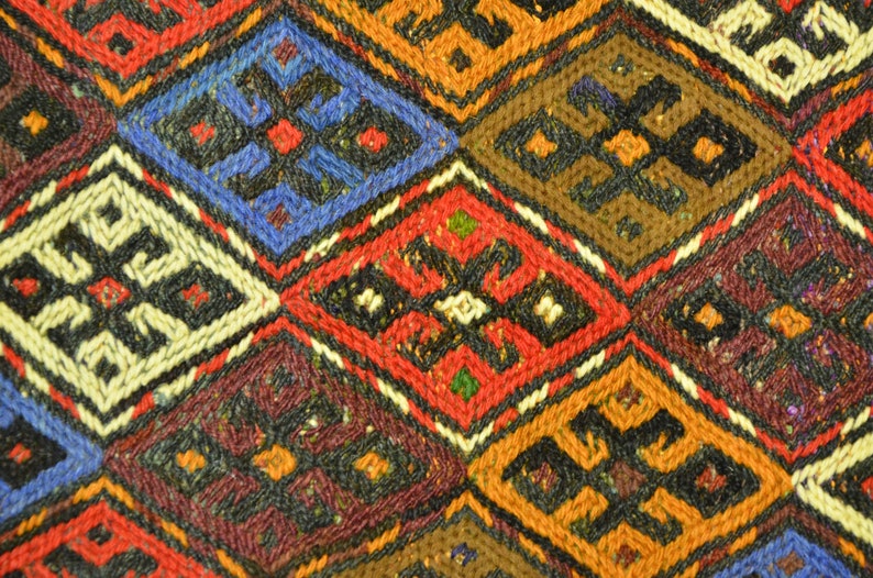 May include: Close-up of a woven textile with a repeating diamond pattern. The design features various colors, including red, blue, orange, brown, and white. Each diamond contains a smaller, contrasting geometric shape.