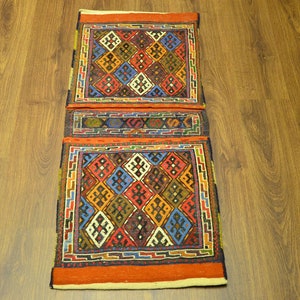 May include: A rectangular, woven textile with a geometric pattern. The design features diamond shapes in red, blue, yellow, and white, framed by a border of blue and white. The textile has a red border.