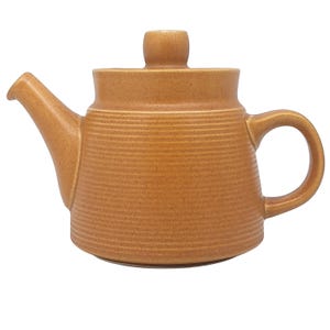May include: A tan ceramic teapot with a lid and handle. The teapot has a spout and a rounded body with horizontal textured lines. The lid has a small knob on top. The teapot is designed for brewing tea.