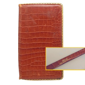 May include: A rectangular, brown leather wallet with a textured, crocodile-like pattern. The wallet has a gold-colored trim around the edges. A smaller inset shows a matching leather strap with the text "ORLIK OLD BOND STREET".