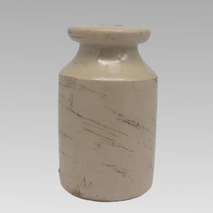 May include: A cylindrical off-white ceramic jar with a wide, flat-topped rim and a narrow neck. The exterior surface features a smooth, glossy finish with visible horizontal and diagonal brown scratch marks and weathered texture throughout the body.