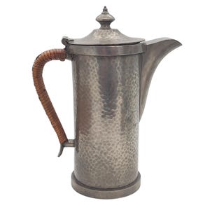 May include: A silver hammered pewter coffee pot with a brown woven handle.