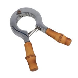 May include: A chrome nutcracker with bamboo handles. The nutcracker features a spring and a curved design. The handles are light brown and have a bamboo texture. It is designed for cracking nuts.