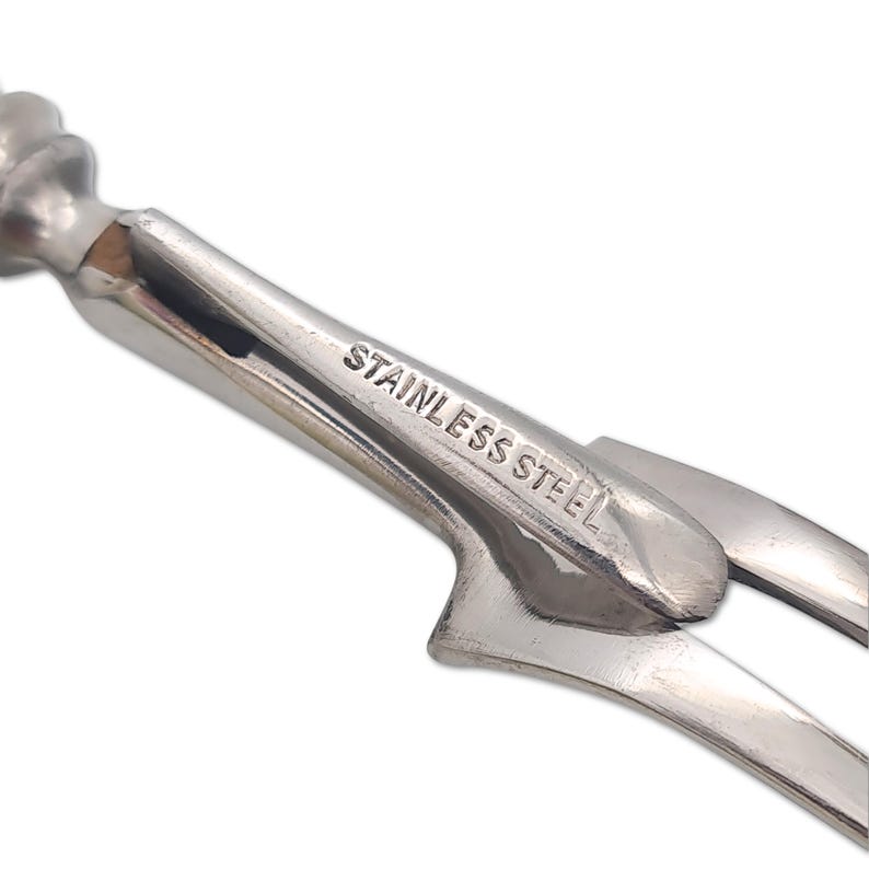 May include: A close-up of a stainless steel corkscrew. The text "STAINLESS STEEL" is stamped on the metal. The corkscrew has a spiral design and a lever arm.