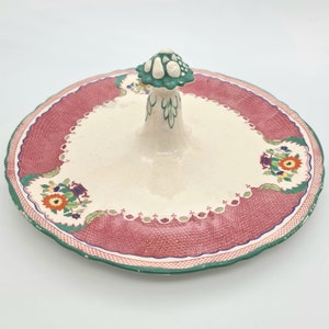 May include: A vintage ceramic serving plate with a raised handle in the shape of a mushroom. The plate has a red and white floral design with green accents.