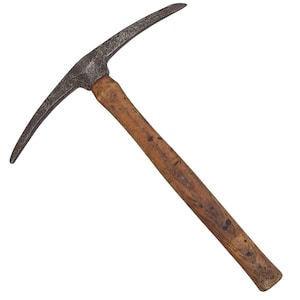 May include: A vintage pickaxe with a weathered wooden handle and a dark, metallic head. The pickaxe head has a curved, pointed end and a flat, chisel-like edge. The wooden handle shows signs of wear and age.