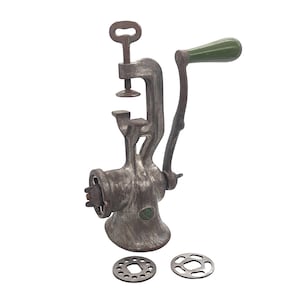May include: An antique, silver-toned meat grinder with a green handle and a clamp for securing it to a surface. Two metal grinding plates are included. The grinder has a vintage aesthetic.