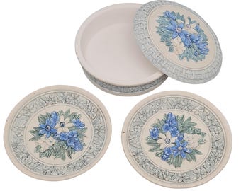 May include: A cream-colored trinket box with a matching lid and two coasters. The lid and coasters feature a raised floral design with blue and white flowers. The box and coasters have a woven-like border.