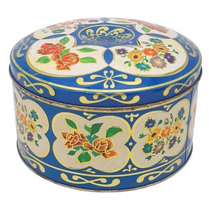 May include: A round, blue tin with a lid. The tin is decorated with floral designs in red, yellow, orange, and purple. The lid and sides have a gold trim. The tin is likely used for storage or as a decorative item.