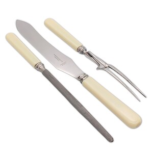 May include: A set of antique silverware, including a knife, a fork, and a sharpening steel. The knife and fork have ivory-colored handles and silver accents. The sharpening steel is a dark gray color.