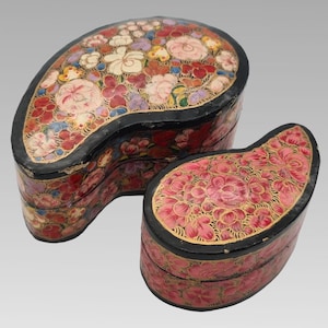 May include: Two paisley-shaped lidded boxes with black edges and intricate hand-painted floral patterns. The larger box features a multi-coloured palette of red, white, and purple flowers, while the smaller box displays a monochromatic pink floral design.