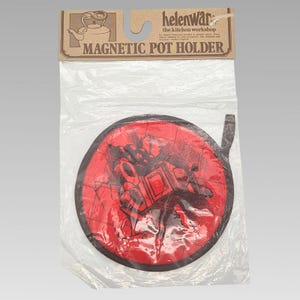 May include: A red and black magnetic pot holder in a clear plastic package. The pot holder is circular with a black border and a graphic design. The packaging reads "MAGNETIC POT HOLDER" and "helen ware the kitchen workshop."