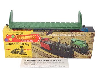 Peut inclure: Maquette de wagon plat à cloison verte avec le texte "BURLINGTON NORTHERN" et "ROUNDHOUSE Products" sur la boîte. Le kit comprend des camions et des coupleurs. La boîte présente des images de modèles de trains.