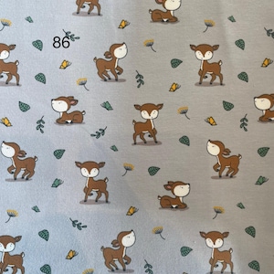Pode incluir: Um tecido cinza claro com um padr&atilde;o repetido de veados castanhos com rostos brancos, folhas verdes e flores amarelas. O n&uacute;mero "86" est&aacute; impresso no canto superior esquerdo. Ideal para roupas infantis ou decora&ccedil;&atilde;o de ber&ccedil;&aacute;rio.