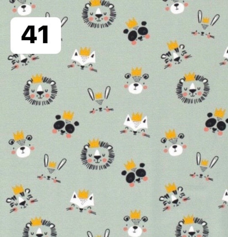 Pode incluir: Um tecido verde claro com um padr&atilde;o repetido de animais de desenho animado usando coroas. Os animais incluem le&otilde;es, pandas, raposas, tigres e coelhos. O n&uacute;mero "41" est&aacute; em uma caixa branca no canto superior esquerdo.