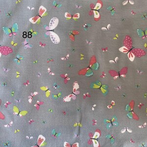 Pode incluir: Tecido cinza coberto por um padr&atilde;o de borboletas coloridas. As borboletas s&atilde;o de v&aacute;rios tamanhos e cores, incluindo rosa, branco, verde e amarelo. O n&uacute;mero "88" est&aacute; impresso no tecido.