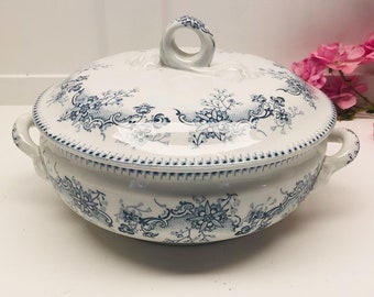 May include: A white ceramic serving dish with a blue and white floral pattern. The dish has a lid with a knob on top.