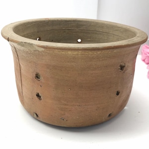 Op de afbeelding: Handgemaakte terracotta-kleurige keramische bloempot met een brede, afgeronde rand en drainagegaten. De pot heeft een licht getextureerd oppervlak en een rustieke uitstraling, geschikt voor binnen of buiten.