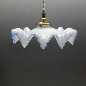 Może przedstawiać: Biały szklany klosz lampy wiszącej z falistą, karbowaną krawędzią wykończoną na niebiesko. Klosz jest przymocowany do metalowej oprawy w kolorze mosiądzu ze skręconym białym przewodem z tkaniny biegnącym w górę od środka lampy.