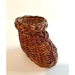 May include: A small, brown wicker basket shaped like a shoe. The basket has a red woven detail around the top and sides.
