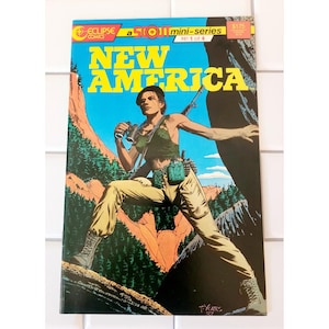 May include: A comic book cover for "New America" by Eclipse Comics. The cover features a woman with binoculars, a rifle, and military gear, set against a mountainous backdrop. The title is in large yellow letters. The comic is labeled as mini-series No. 1 of 4.