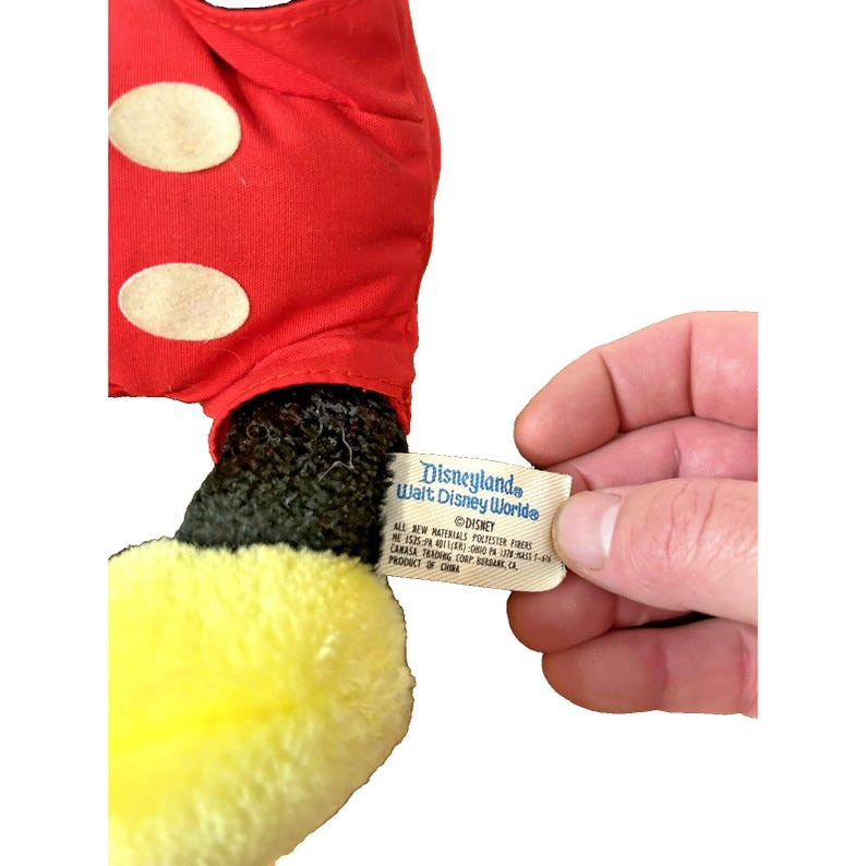 May include: A vintage Mickey Mouse plush toy, featuring a red outfit with white polka dots and yellow gloves. The tag reads "Disneyland Walt Disney Worlde". The plush is made of soft materials.