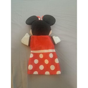 May include: A Minnie Mouse hand puppet. The puppet has black ears, a red and white polka dot dress, and white sleeves. A red bow is on top of the head. The puppet is made of soft fabric.