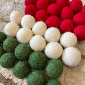 May include: A Christmas tree ornament made of felt balls in red, white, and green. The balls are arranged in a pyramid shape, with the red balls at the top, the white balls in the middle, and the green balls at the bottom.