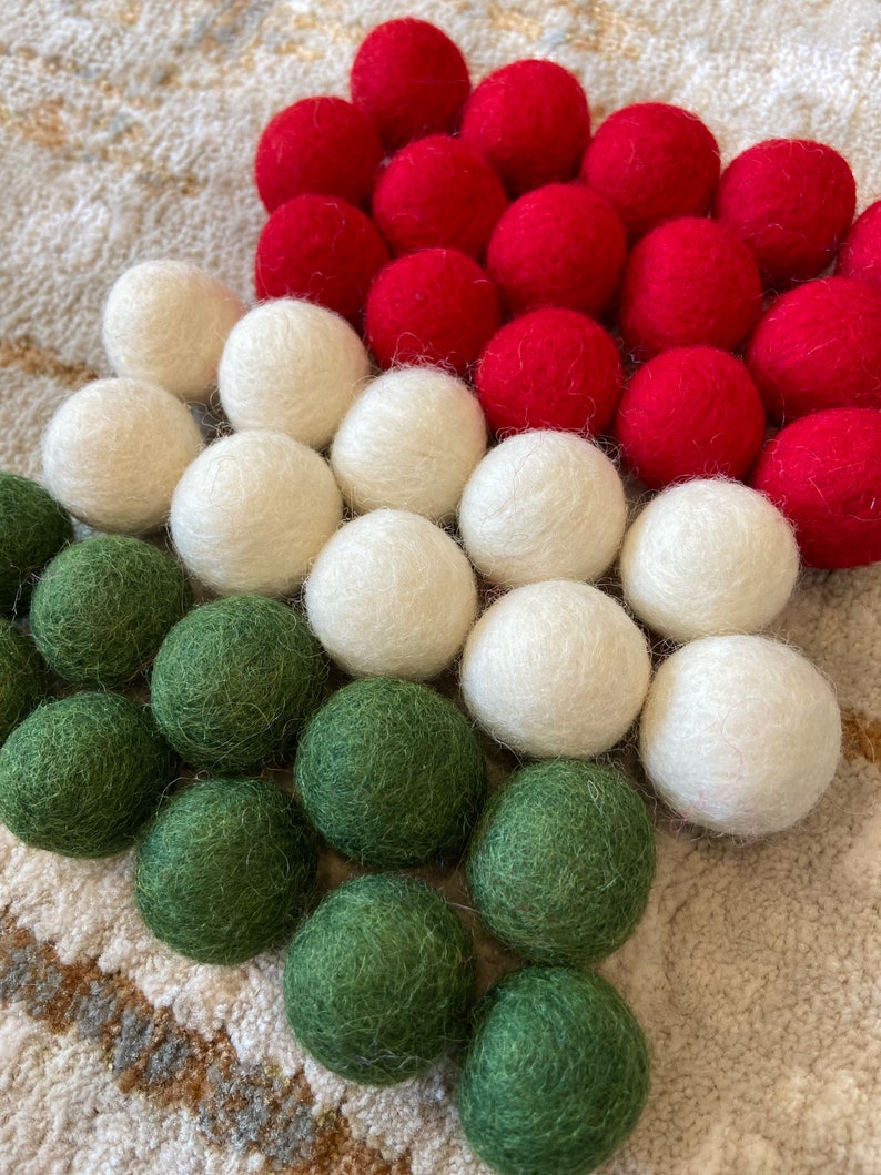 May include: A Christmas tree ornament made of felt balls in red, white, and green. The balls are arranged in a pyramid shape, with the red balls at the top, the white balls in the middle, and the green balls at the bottom.