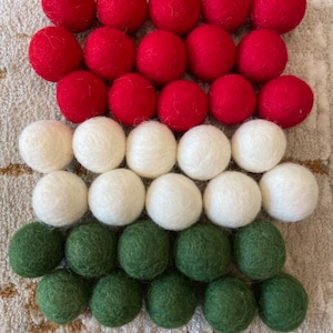 May include: A collection of felt balls in red, white, and green. The balls are arranged in three rows, with the red balls on top, the white balls in the middle, and the green balls on the bottom.