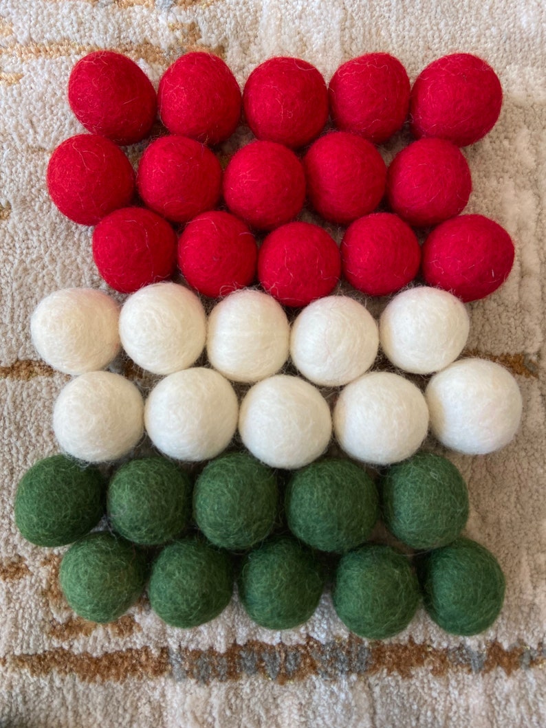 May include: A collection of felt balls in red, white, and green. The balls are arranged in three rows, with the red balls on top, the white balls in the middle, and the green balls on the bottom.