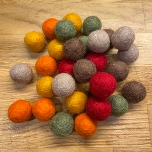 Könnte beinhalten: Ein Haufen Filzkugeln in verschiedenen Farben, darunter Rot, Orange, Gelb, Grün, Braun und Grau. Die Kugeln sind in einem zufälligen Muster angeordnet und alle etwa gleich groß.