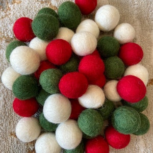 May include: A pile of felt balls in red, white, and green colors. The balls are arranged in a random pattern.