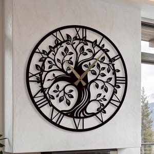 Può includere: Un grande orologio da parete circolare in metallo nero con un intricato design ritagliato di un albero con rami e foglie estesi. Il quadrante dell'orologio include numeri romani lungo il bordo e due lancette sottili di colore chiaro.