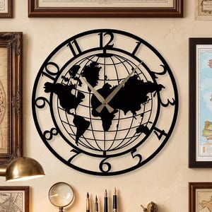 May include: A circular black metal wall clock featuring a world map silhouette and a grid of longitude and latitude lines. The clock face displays large black Arabic numerals from one to twelve around the outer edge with silver-toned clock hands.