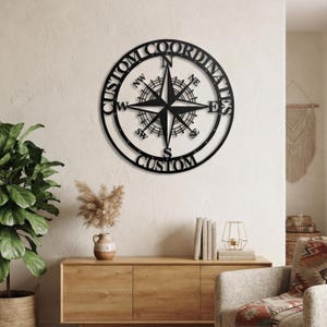 May include: A circular black metal wall art piece featuring a compass rose design in the centre. The outer ring contains the text CUSTOM COORDINATES at the top and CUSTOM at the bottom. The compass includes directional markers N, S, E, W, NW, NE, SW, SE.