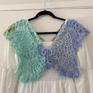 May include: A white crocheted top with a blue and green crocheted shawl. The shawl is made of delicate, lacy stitches and has a scalloped edge.