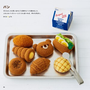 Può includere: Una collezione di prodotti da forno all'uncinetto, tra cui un panino a forma di orso, un croissant e un hot dog, disposti su un vassoio di metallo. Sono presenti anche un cartone di latte vintage e pinze da portata. Il testo è in giapponese.