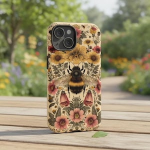 Puede incluir: Funda de teléfono beige con una ilustración detallada de un abejorro rodeado de flores amarillas, rosas y rojas. La funda tiene un estampado floral y un recorte para la cámara. El diseño recuerda al arte botánico vintage.