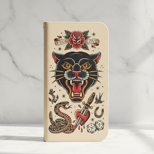 Puede incluir: Cartera color crema con un diseño de tatuaje tradicional. El diseño incluye una cabeza de pantera negra, una rosa roja con una pancarta que dice "TRUE LOVE", una serpiente, una daga a través de un corazón, una ancla, una herradura, dados y una golondrina.