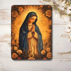 Puede incluir: Una pintura de la Virgen María con una túnica azul y un vestido blanco, con las manos juntas en oración. Está rodeada de rosas amarillas y un halo dorado.
